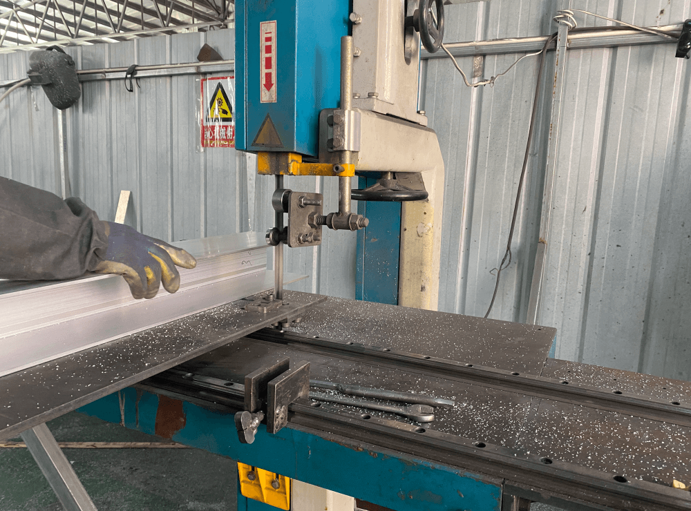 Worker cutting aluminum profiles on an industrial band saw in a truck accessories manufacturing workshop