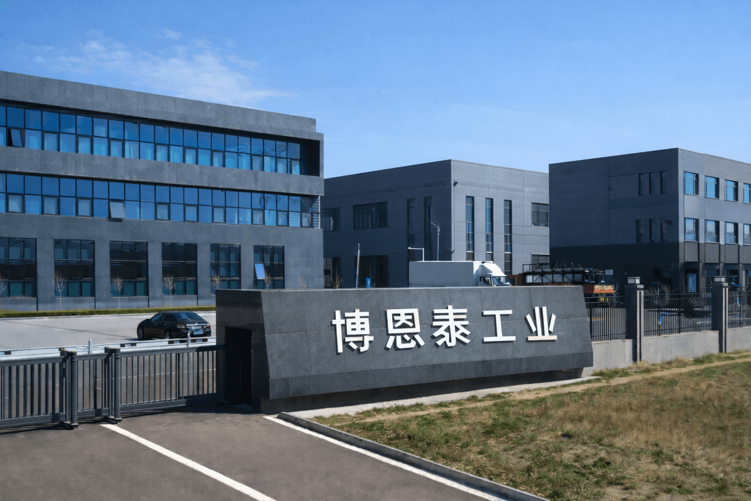 Exterior view of the manufacturing facility entrance with factory buildings and main gate signage