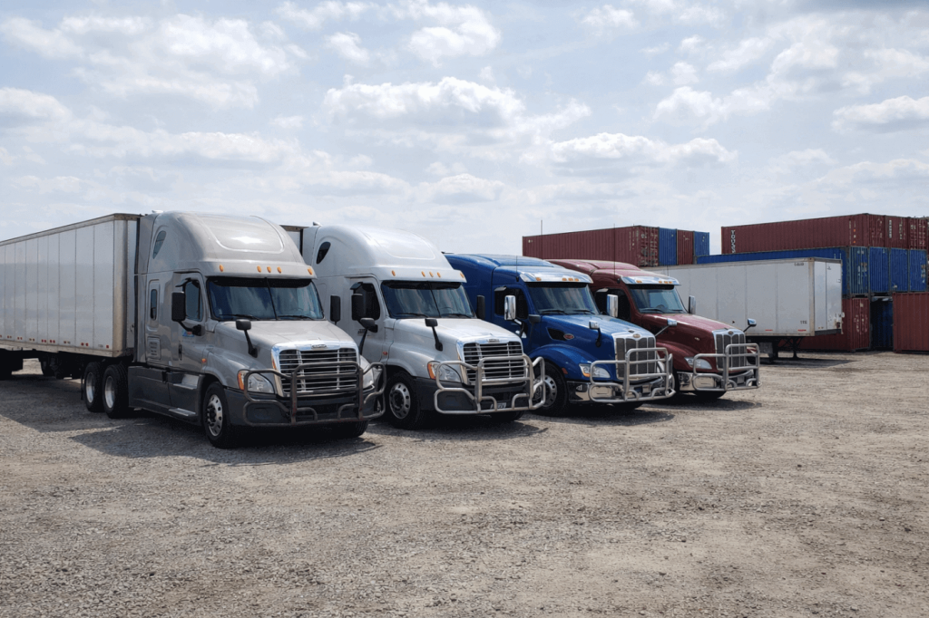Four Class 8 semi trucks parked in a logistics yard equipped with heavy-duty grille guards for front-end protection and fleet durability.