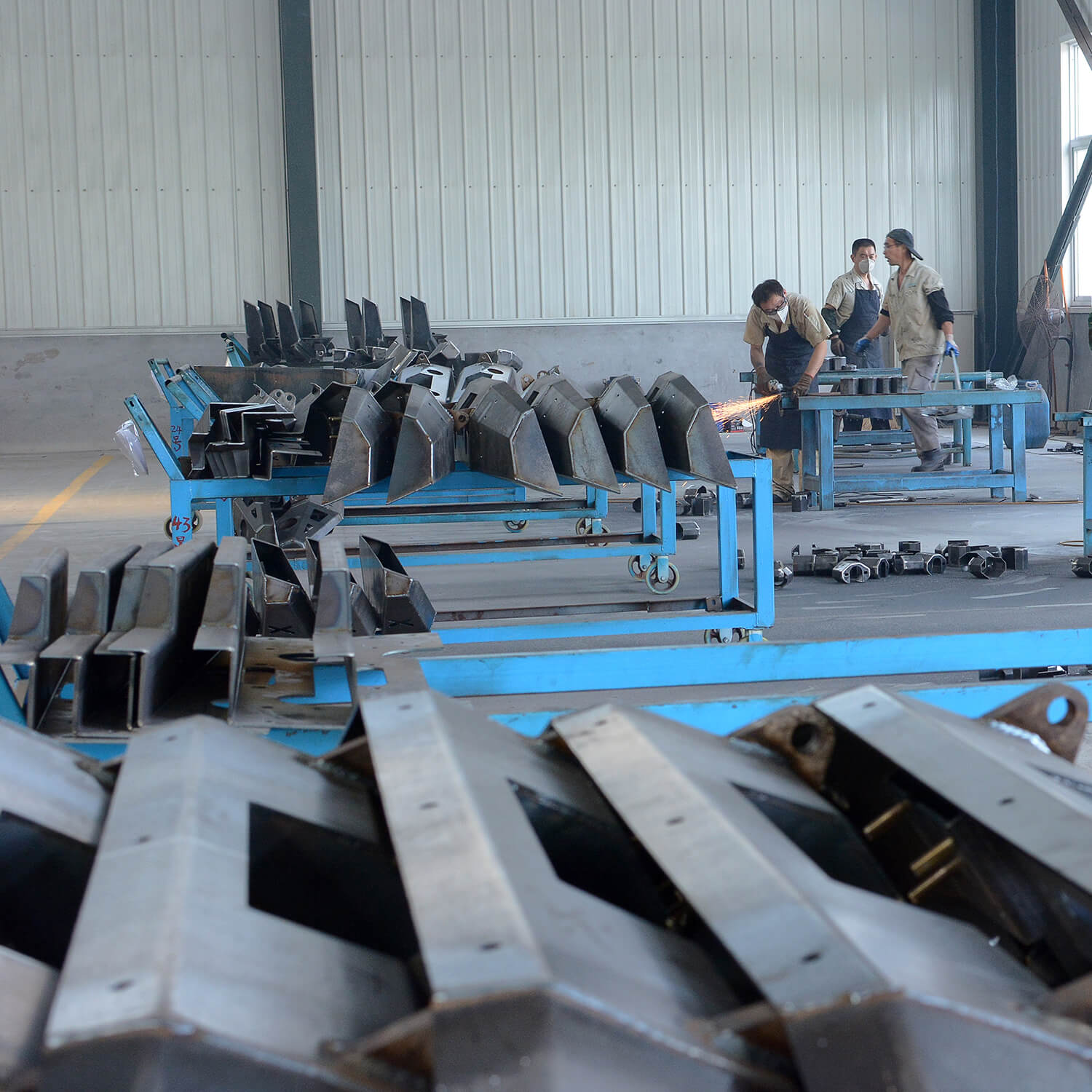 Workers welding and grinding heavy-duty steel structural parts in truck accessory manufacturing workshop