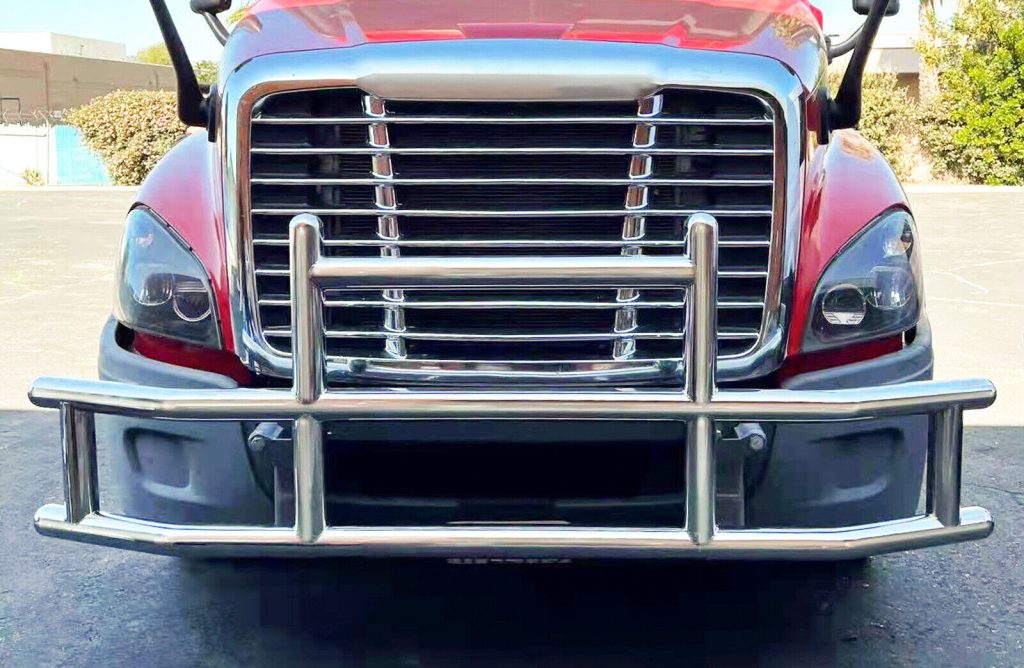Heavy-duty stainless steel grille guard installed on a semi truck providing front-end protection for headlights, grille, and bumper components