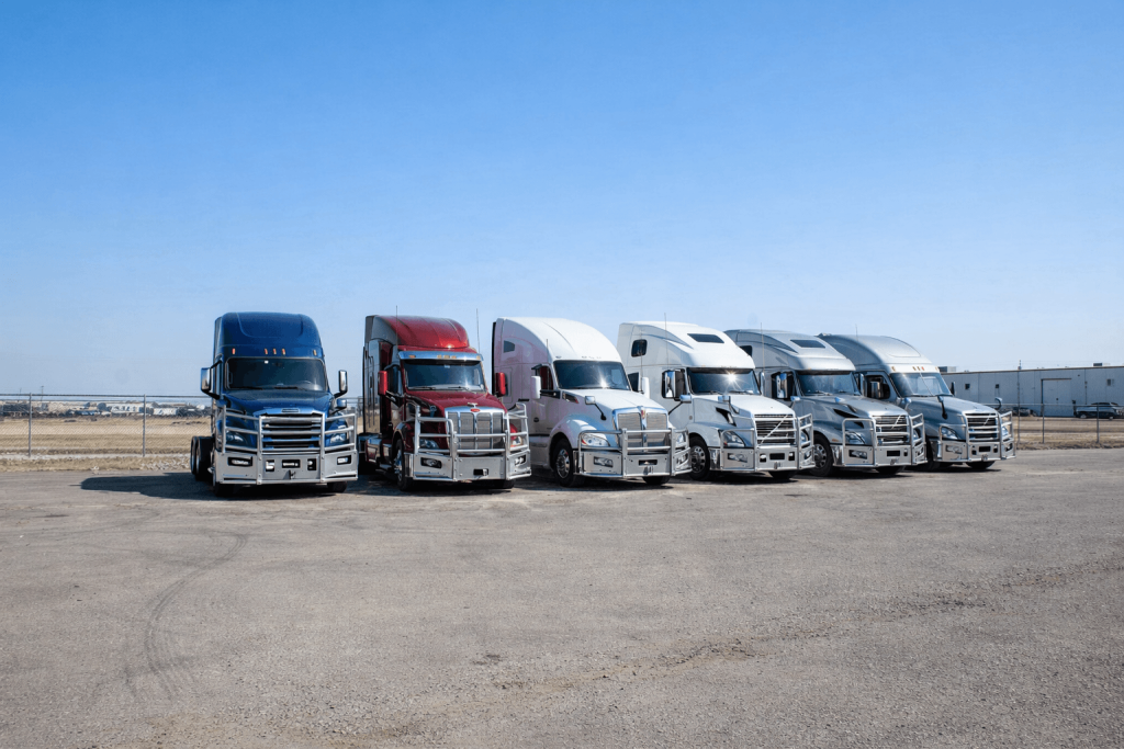 Lineup of modern Class 8 semi trucks equipped with polished semi truck aluminum bumpers parked in an industrial fleet yard